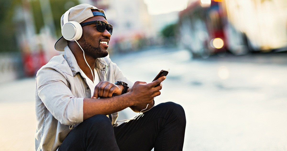 Un uomo con le cuffie ascolta un podcast dallo smartphone, seduto in strada